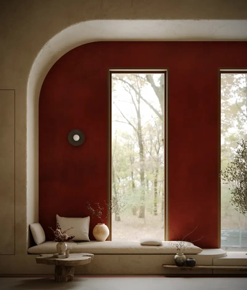 A built-in window seat with linen cushions, clay vases and a timber side table beneath a red arched wall