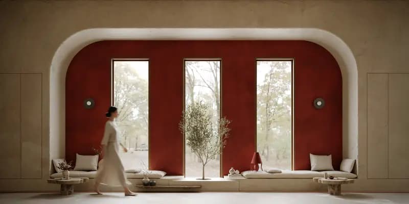 A woman walking past a window seat under a red arched wall with tall windows